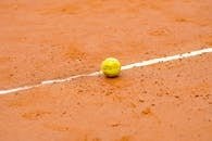 Tennis ball resting on a clay court, marked by a white line, ideal for sports themes.