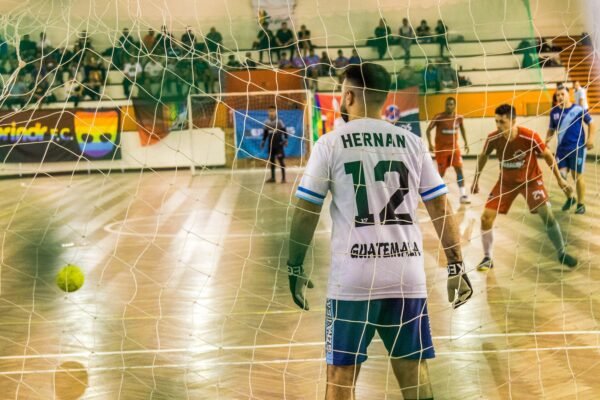 Goalkeeper watches incoming players in an intense indoor soccer match.